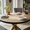 Ronde eikenhouten eettafel met visgraatpatroon en houten kruispoot in een licht, Scandinavisch interieur.