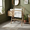 Vrijstaand inklapbaar handdoekrek van duurzaam FSC teak hout in een moderne Scandinavische badkamer met een witte handdoek, houten wastafelmeubel en ronde spiegel