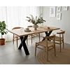 Eikenhouten eettafel met zwart metalen X-poot en houten Wishbone-stijl stoelen in een licht Scandinavisch interieur.