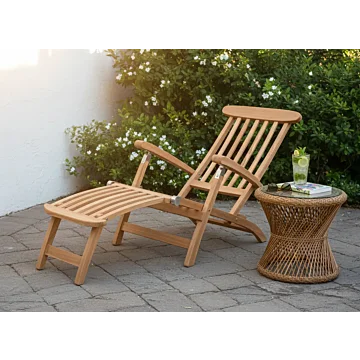 Klassieke teakhouten deckchair met zilverkleurig RVS beslag op een stenen terras, inclusief voetensteun en naast een rotan bijzettafel