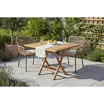 Deze sfeervolle setting illustreert een intiem buitenverblijf, ideaal voor een zomers ontbijt of een ontspannen middag in de tuin. De combinatie van warm teakhout en tactiel vlechtwerk creëert een tijdloze, natuurlijke esthetiek die naadloos aansluit bij 