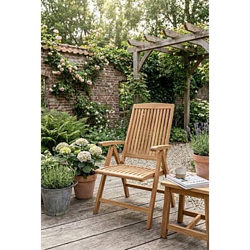 Houten inklapbare tuinstoel en bijzettafel van teak op een vlonder in een sfeervolle tuin met bloemen, een bakstenen muur en een pergola.