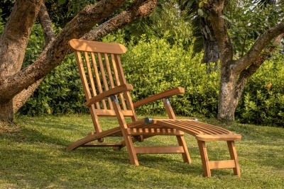 Klassieke teakhouten deckchair met zilverkleurig RVS beslag op een stenen terras, inclusief voetensteun en naast een rotan bijzettafel - alternate view
